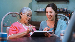 A young sister helping an elderly sister to use her tablet.