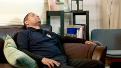 Scéna z videa „Projevuj neselhávající lásku ve službě“. Táta z videa spí na gauči potom, co přišel domů z práce.