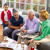 A family hosting an older couple for family worship. The family listens joyfully as the couple show photos and recount experiences.