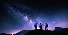 Tres excursionistas en la cima de una montaña viendo el cielo lleno de estrellas.