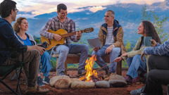 Przyjaciele siedzą wokół ogniska. Jedna osoba gra na gitarze.