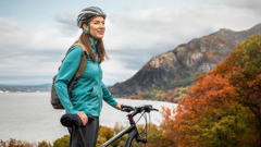 A sister riding a bike stops atop a hill overlooking a lake to enjoy creation.