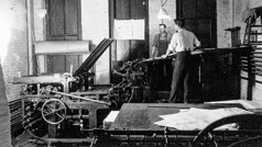 Two brothers operating a flatbed printing press.