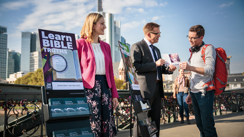 Martori ai lui Iehova vorbesc cu un bărbat lângă căruciorul cu literatură