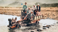 Kathleen, Harvey, and several others riding on a makeshift vehicle across a shallow river.