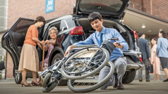 Młody brat rozkłada wózek inwalidzki starszej siostry, a jego mama pomaga jej wysiąść z samochodu.