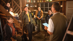 Eine Gruppe von Zeugen Jehovas in einem Keller. Einer von ihnen schaut einen Bruder, der gerade Anweisungen gibt, skeptisch an.