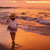 Dok sunce zalazi, sestra šeta plažom i gleda kako talasi zapljuskuju obalu.