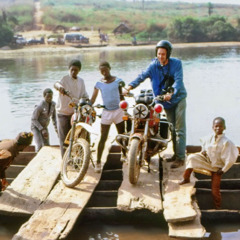 Роберт и други браќа стојат покрај своите мотори додека со сплав минуваат една река.