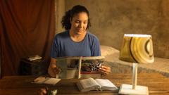 A young sister at her desk, reading the brochure “Answers to 10 Questions Young People Ask.” On the desk are an open Bible, a notepad, and a pen.