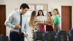 Uma jovem conversando com um grupo de irmãs. Ela presta atenção em um irmão solteiro que está limpando o Salão do Reino