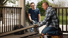 A young brother learning from an older brother how to repair a wooden deck.