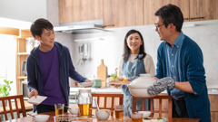 A young brother helping his parents set a dinner table before they eat a meal together.