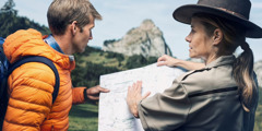 A young man getting help from a park ranger. She uses a map to show him which route to take to get to his destination, the top of a mountain.