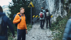路邊有個「小心落石」的警示牌。年輕人停住，其他登山客卻繼續往前走。
