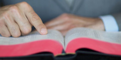 Un homme lit la Bible tout en suivant le texte avec son doigt.