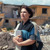 Сестра стоит рядом с домом, который был разрушен стихийным бедствием, и держит в руках Библию. На её лице спокойствие.