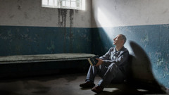 A brother in a prison cell holding a Bible and looking out the window.