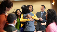 A sister at the Kingdom Hall, hugging a sister who has just been reinstated. Others happily gather around them.