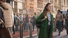 A sister calmly looking ahead as she walks past a group of protesters on a busy city street.