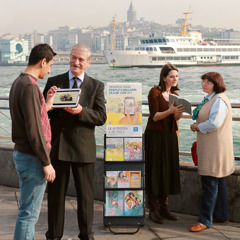 Jehovah’s Witnesses stand by a literature display cart and share in public witnessing