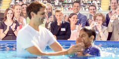 Varias personas ven cómo se bautiza un joven, mientras otro joven mira pensativo