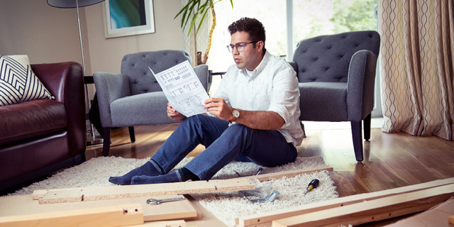 Un hombre leyendo las instrucciones del fabricante para armar un mueble.