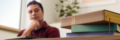 A man looking contemplatively at a Bible and other books on his desk.