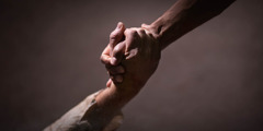 A person reaching down and grasping someone’s hand.