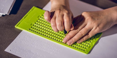 Transcribing a book into braille, using a writing slate and stylus.