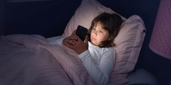 Una niña mira su celular en la noche acostada en su cama.