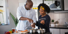 Sepasang suami istri sedang memasak bersama dan terlihat bahagia.