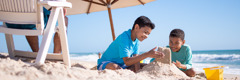 Children building a sandcastle at the beach as their father sits nearby.