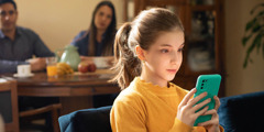 Uma menina vidrada no seu celular enquanto seus pais a observam e esperam, sentados à mesa de café da manhã.