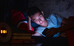 En dreng ligger i sin seng og er helt opslugt af sin telefon, selvom klokken er over 1 om natten.