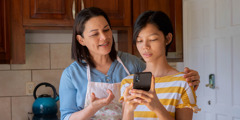 A teenage girl showing her mother something on a smartphone.