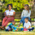 Two mothers of different races sitting on a park bench, smiling and talking while their two young sons play together.