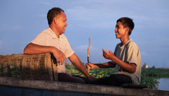 A father and his teenage son conversing happily in a boat.