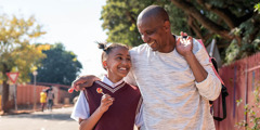 Otac i ćerka tinejdžerskog uzrasta nasmejani šetaju ulicom.
