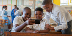 Три малки момчета в училище гледат съсредоточено екрана на телефон.