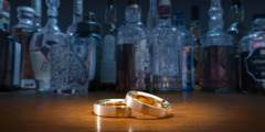 Two wedding rings and various bottles of alcohol on a table.