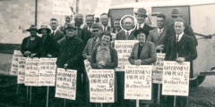 Broder Fred McAuley står tillsammans med en grupp vittnen som håller upp skyltar för att bjuda in till broder Rutherfords tal ”Herradömet och freden” 1939.