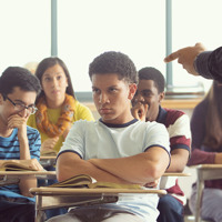 A student sitting in class, being reprimanded by his teacher.