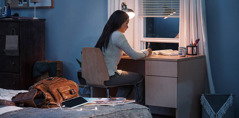 Seorang gadis belajar di meja belajar di kamarnya. Dia menaruh ransel, HP, dan majalah di belakangnya.