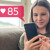 一个年轻女孩微笑着在看自己的手机，她在社交平台上得到85个赞