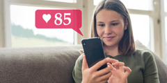 ایک نوجوان لڑکی اپنے فون کو دیکھ کر مسکرا رہی ہے۔ اُس کی پوسٹ پر 85 لائکس ہیں۔‏