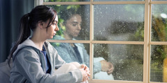 Skľúčené dospievajúce dievča sa v daždi pozerá cez okno