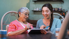 Seorang gadis remaja membantu seorang wanita lansia menggunakan tablet elektronik.