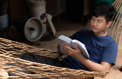Een jongen ligt in een hangmat de Bijbel te lezen.