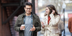 A young man and woman conversing happily as they walk together on a city street.
